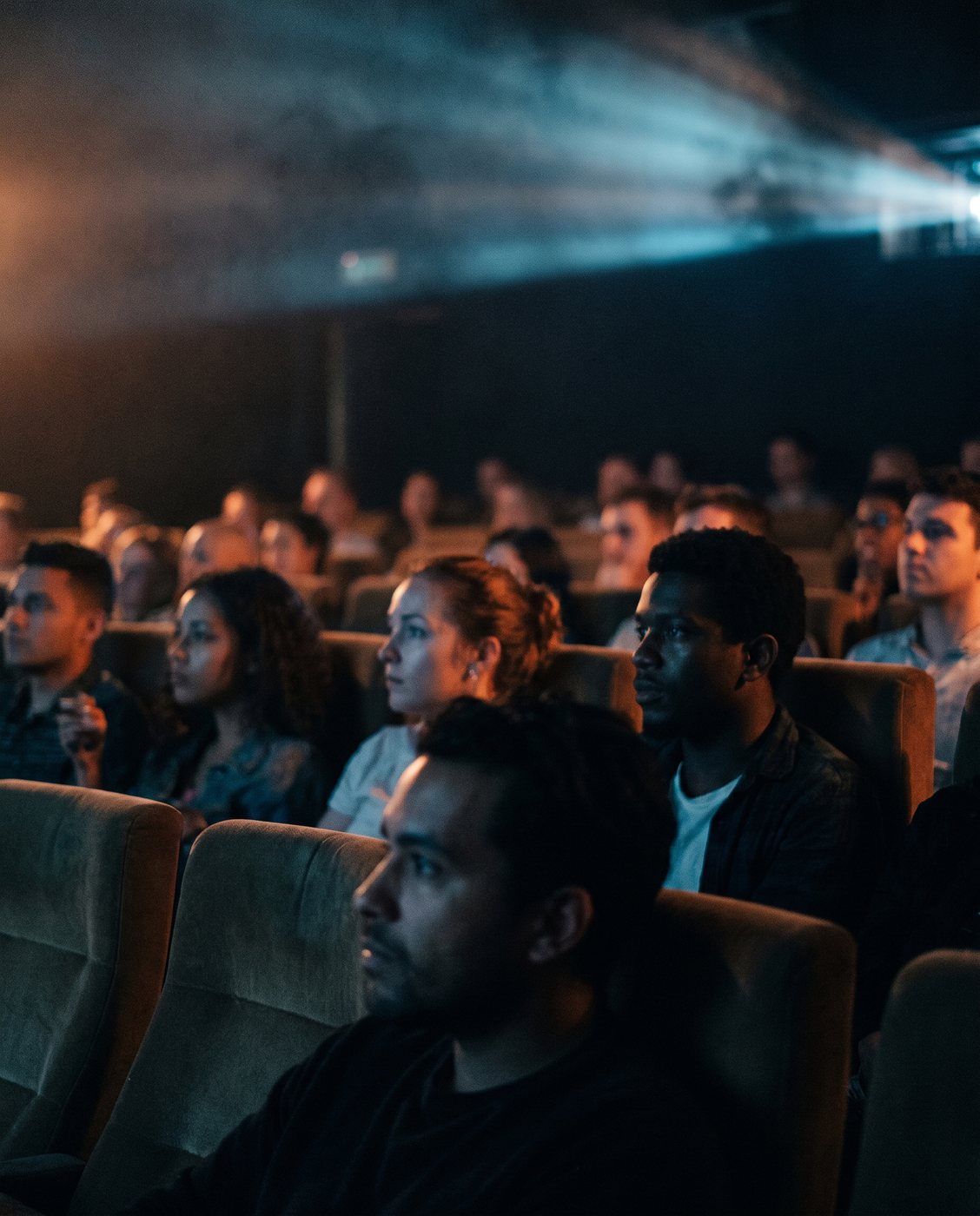 A theater audience in the dark, lit by the glow of the screen